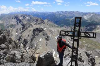 Mann steht bei Gipfelkreuz mit Blick über Alpen