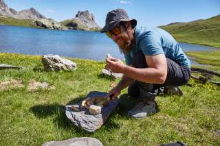 Mann sitzt an Bergsee und isst Brot und Käse