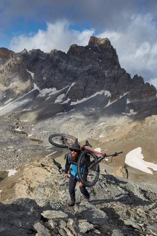 Mann mit Bike auf den Schultern läuft Berg hoch