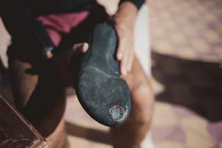 Nahaufnahme einer Hand, die einen schwarzen Kletterschuh mit einem Loch an der Sohle hält.