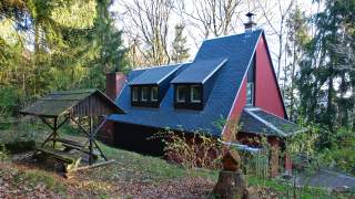 Ein rotes Haus mit spitzem Dach - erinnert an ein Hexenhäuschen - mitten im Wald.