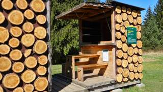 Ein kleines Biwak verkleidet mit runden Holzplatten, als hätte man Scheiben von einem Stamm abgesägt.