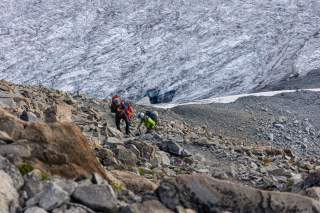 Menschen steigen durch felsiges Gelände oberhalb von Gletscher auf