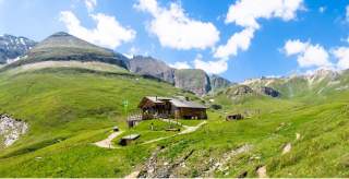 Hütte in grüner Almlandschaft mit Gipfeln im Hintergrund