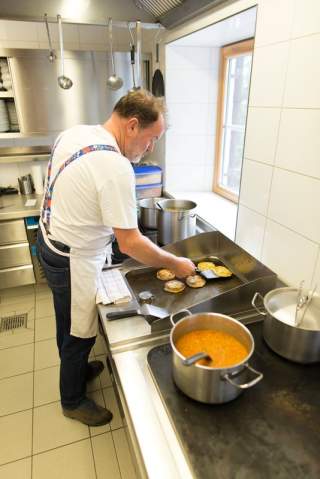 Ein Mann steht in einer Industrieküche. Er beugt sich über einen großen Grill und bratet dort Kaspressknödel an.