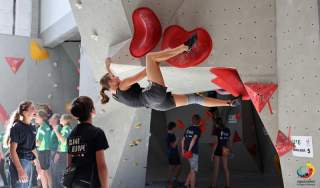 Eine Schülerin klettert an einer Indoor-Boulderwand, während mehrere Personen im Hintergrund zuschauen.