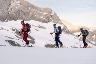 Drei Personen auf Skitour mit felsigem Gipfelaufbau im Hintergrund