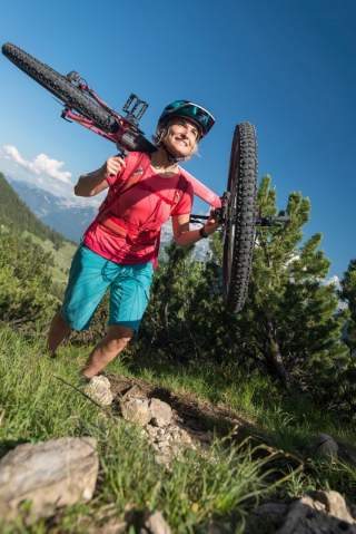 Frau trägt Mountainbike schmalen Bergpfad hoch