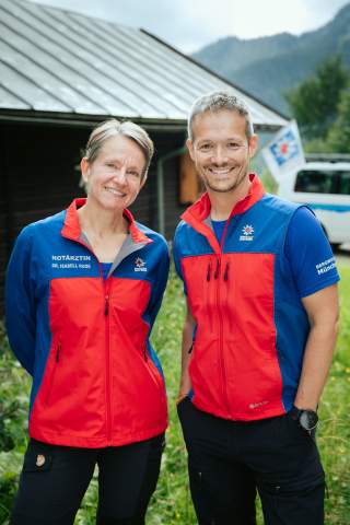 Frau Doktor Isabell Ruoß und Herr Henrik Vogel stehen vor ihrer Diensthütte. Sie tragen ihre typische blau-rote Kleidung.