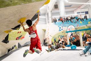 Person beim Bouldern in einer Halle mit Zuschauer*innen