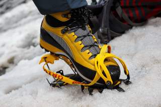 Nahaufnahme eines gelben Bergstiefels mit Steigeisen auf Schnee.