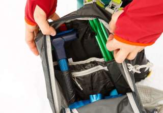 Der Blick in einen geöffneten Skitourenrucksack zeigt den Stiel einer Lawinenschaufel und eine gefaltete Lawinensonde.