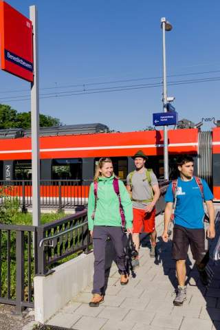 Drei Menschen laufen in Wander-Outfits am Bahnhof