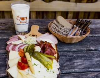 Ein Glas Milch, ein Brotkorb und eine Wurst- und Käseplatte.