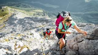 Drei Menschen klettern an Stahlseil felsigen Berg hoch