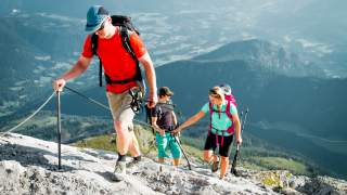 Drei Menschen wandern mit Stahlseil gesicherten Fels hinauf