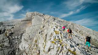Drei Menschen wandern über felsige Platten auf Gipfel zu