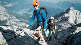 Zwei Menschen laufen an Drahtseil in alpinem Gelände