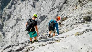 Zwei Menschen steigen auf ausgesetzter Querung am Berg
