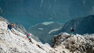 Drei Menschen wandern am Watzmann mit Blick auf den Königssee