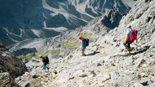 Drei Wandernde steigen steile, schotterige Rinne hinab