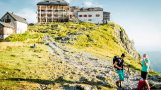 Zwei Menschen stehen vor Berghütte und trinken etwas