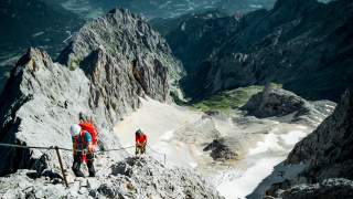 Zwei Menschen steigen an Stahlseil zu Gipfel auf