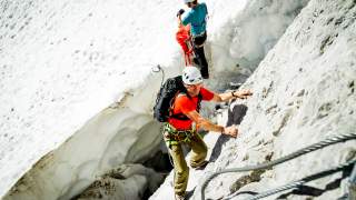Zwei Menschen überwinden Randkluft eines Gletschers
