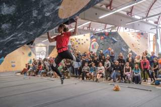 Junge Frau an Boulderwand vor Zuschauer*innen