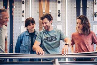 Vier Personen begutachten und vergleichen Skier in einem Geschäft mit Skiausrüstung an der Wand.