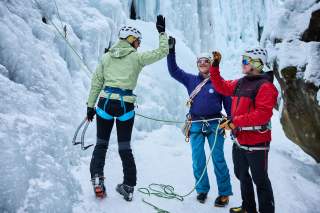 Drei Menschen an Eiswasserfall schlagen ein