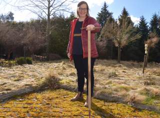 Frau steht in Garten mit historischem Eispickel in der Hand