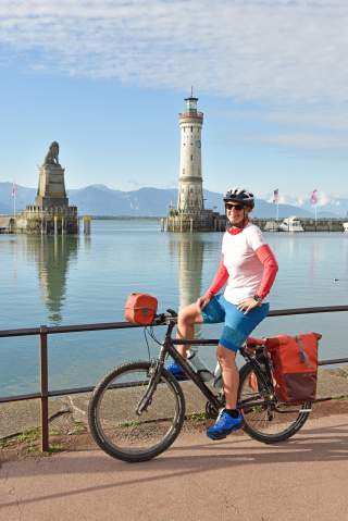 Frau sitzt auf Trekkingrade vor der Hafeneinfahrt von Lindau am Bodensee