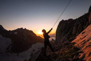Frau sichert im Hochgebirge bei Sonnenuntergang Frau sichert im Hochgebirge bei Sonnenuntergang