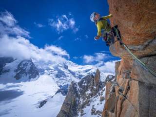 Frau klettert an Fels vor hochalpiner Landschaft