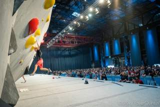 Junger Mann an Boulderwand vor Publikum