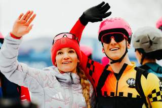 Zwei Menschen winken in Richtung Publikum.