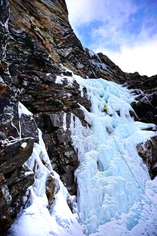 Vereister Wasserfall mit kleinem Eiskletterer am Seil gesichert