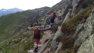2 Personen mit Fahrradhelmen tragen ihre Mountainbikes einen felsigen Bergpfad bergauf