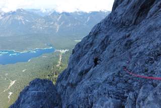 Mensch klettert schattige Wand rauf, Ausblick auf See und Berge