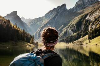 Frau steht an See und bewundert Bergkulisse