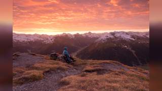 Person wandert auf Berggrat, der sich durchs Bild zieht