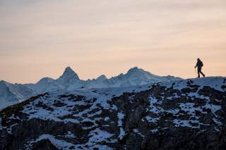 Person wandert über Grat, im Hintergrund ragen markante schneebedeckte Gipfel auf