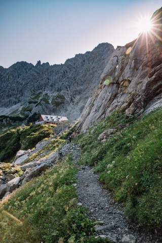 Blick auf Berghütte während die Sonne hinter den Gipfeln untergeht