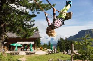 Kind schaukelt, im Hintergrund Berghütte