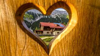 Berghütte gesehen durch herzförmig ausgeschnittenes Brett