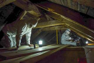 Zwei Menschen in Schutzkleidung reinigen den Dachboden einer Berghütte.