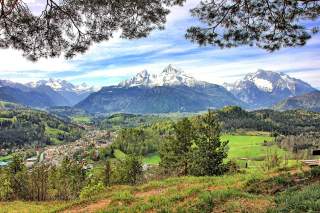 Blick über ein Tal: Der Frühling hat Einzug gehalten und die Laubbäume sind frisch-grün, auf den markanten Bergen liegt noch Schnee.