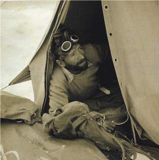Eine alte Schwarzweißfotografie vom Bergsteiger Hermann Buhl in einem Expeditionszelt, die Gletscherbrille in die Haare geschoben.