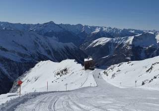 Hütte am Rande der Skipiste vor grandiosem Bergpanorama